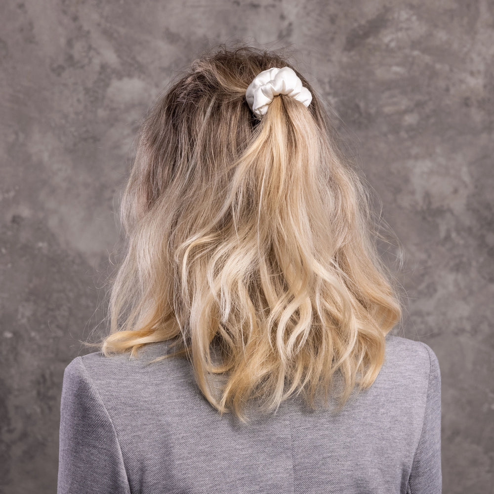 
                  
                    A blonde-haired woman, view from the back, with stylish ponytail is wearing Malkiele designer white silk-covered coil scrunchie, name Grace.
                  
                