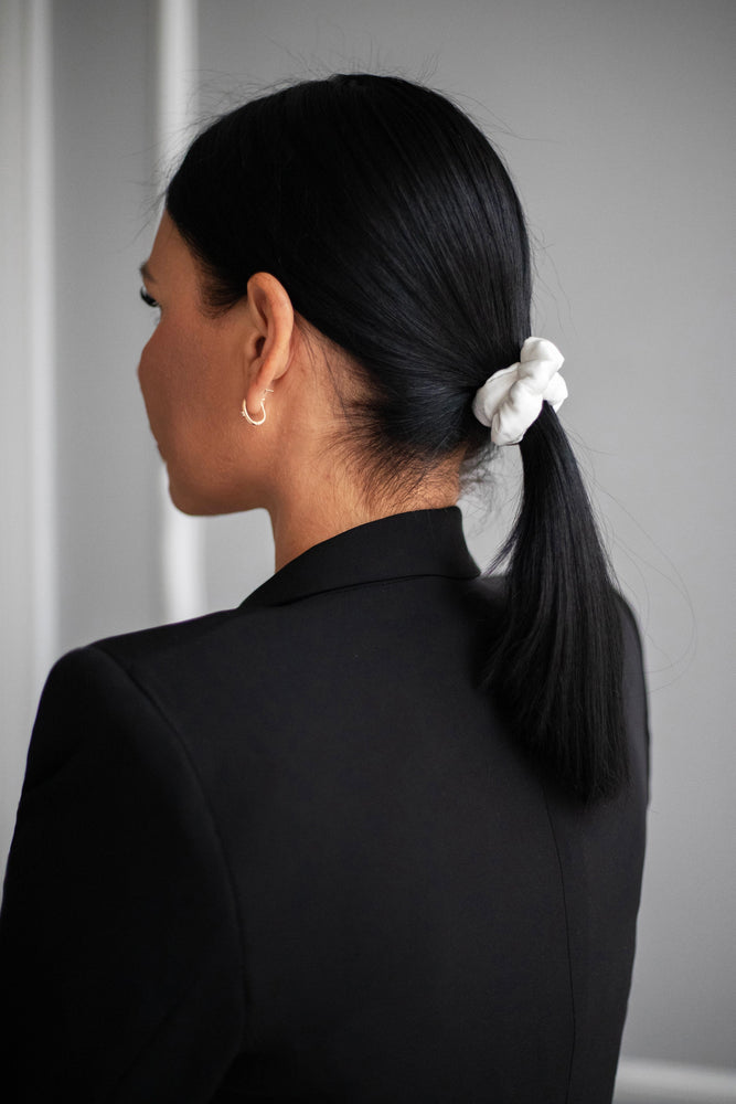 
                  
                    A dark-haired woman, view from the back, with stylish ponytail is wearing Malkiele designer white silk-covered coil scrunchie, name Grace.
                  
                