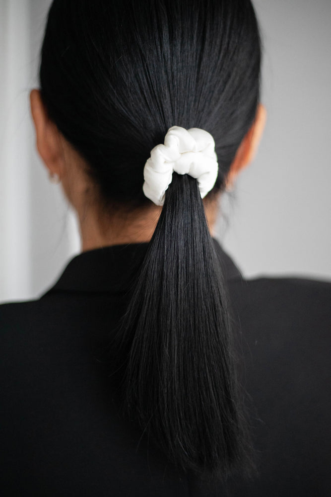 
                  
                    A dark-haired woman, view from the back, with stylish ponytail is wearing Malkiele designer white silk-covered coil scrunchie, name Grace.
                  
                