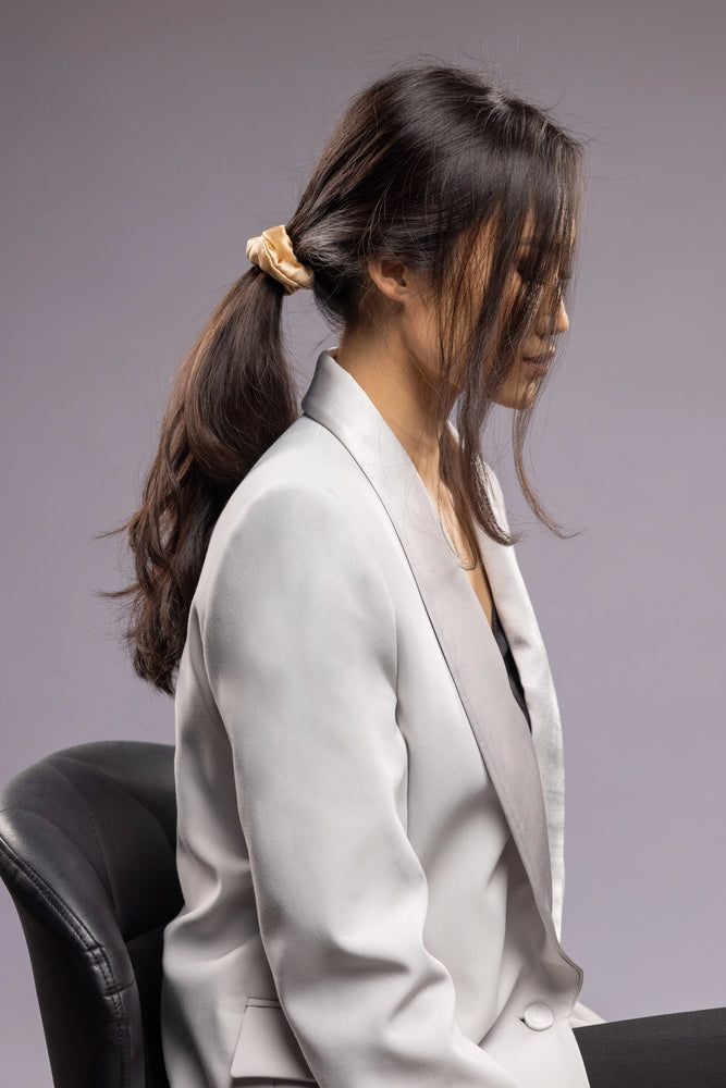 
                  
                    A black-haired woman, view from the side, with stylish ponytail is wearing Malkiele designer beige silk-covered coil scrunchie, name Grace.
                  
                