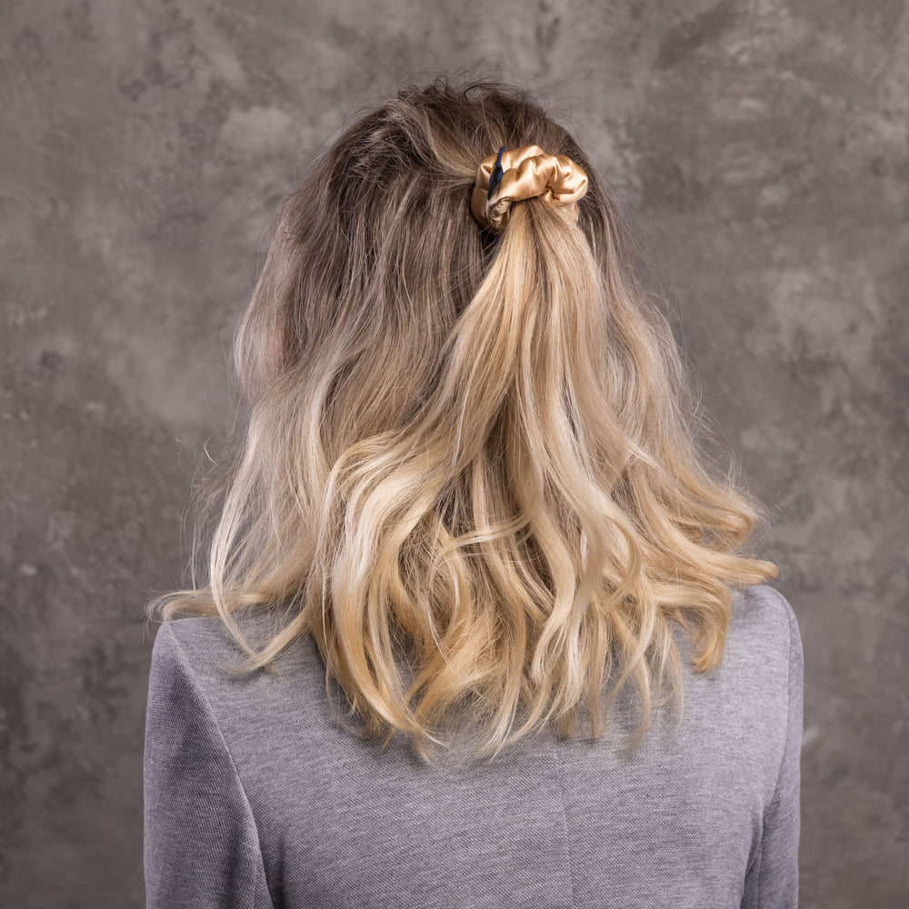 
                  
                    A blonde-haired woman, view from the back,  with stylish ponytail is wearing Malkiele designer beige silk-covered coil scrunchie, name Grace.
                  
                