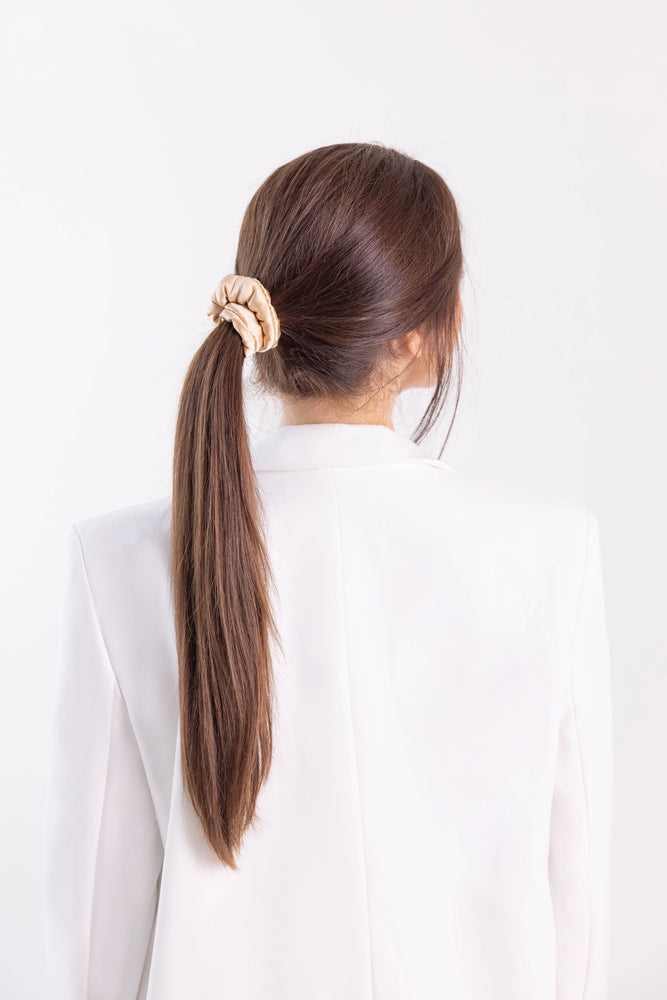 
                  
                    A dark-haired woman, view from the back, with stylish ponytail is wearing Malkiele designer beige silk-covered coil scrunchie, name Grace.
                  
                