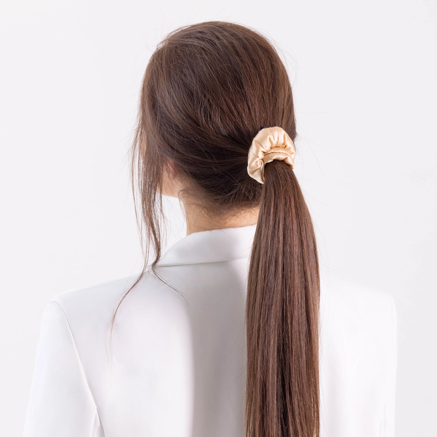 
                  
                    A dark-haired woman, view from the back, with stylish ponytail is wearing Malkiele designer beige silk-covered coil scrunchie, name Grace.
                  
                