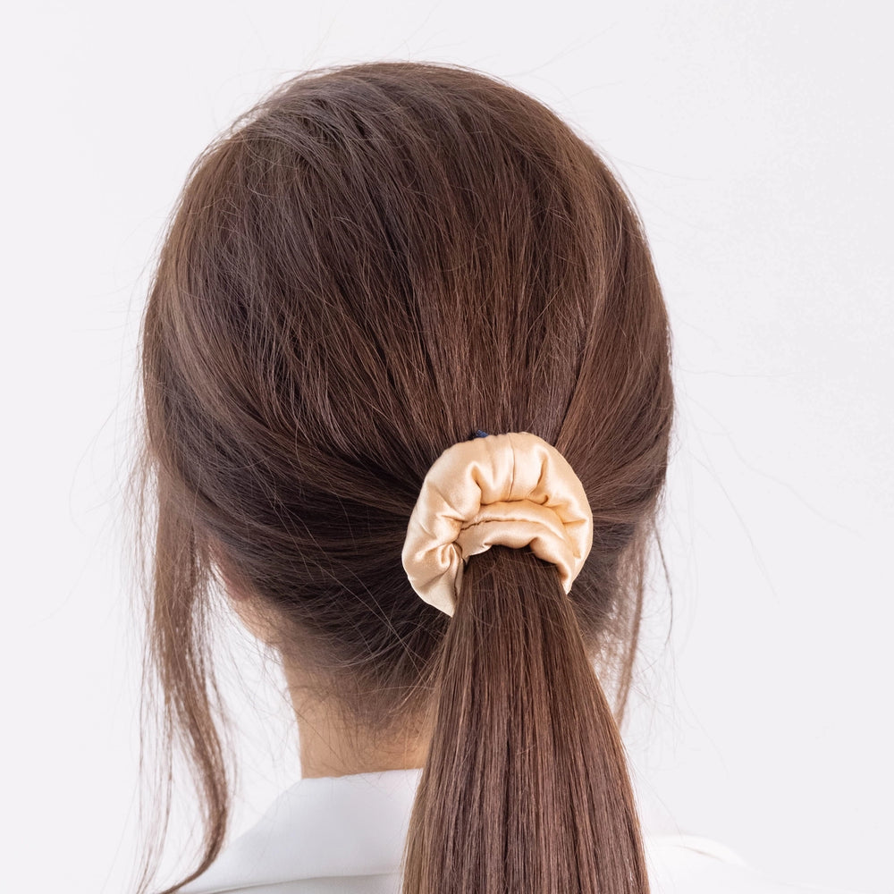 
                  
                    A dark-haired woman, view from the back, with stylish ponytail is wearing Malkiele designer beige silk-covered coil scrunchie, name Grace.
                  
                