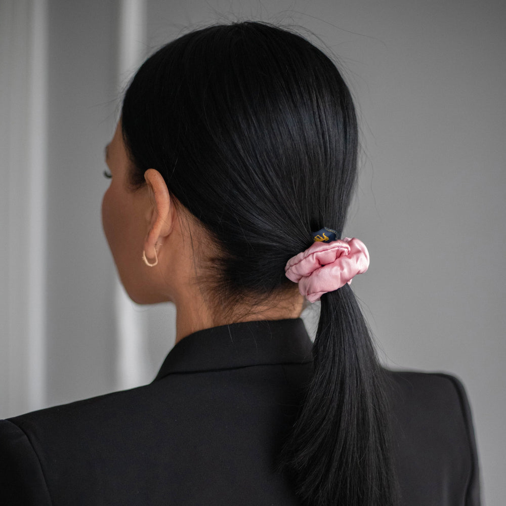 
                  
                    A black-haired woman, view from the back, with stylish ponytail is wearing Malkiele designer pink silk-covered coil scrunchie, name Grace.
                  
                