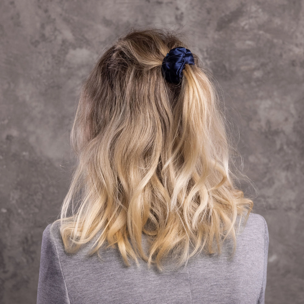 
                  
                    A blonde-haired woman, view from the back, with stylish ponytail is wearing Malkiele designer navy blue silk-covered coil scrunchie, name Grace.
                  
                