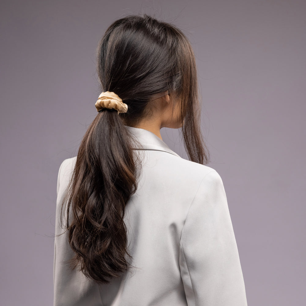 
                  
                    A black-haired woman, view from the back, with a long and stylish ponytail is wearing Malkiele designer beige silk-covered coil scrunchie, name Grace.
                  
                