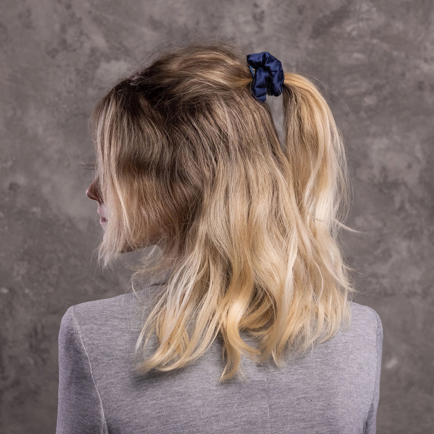 
                  
                    A blonde-haired woman, view from the back,  with stylish ponytail is wearing Malkiele designer navy blue silk-covered coil scrunchie, name Grace.
                  
                