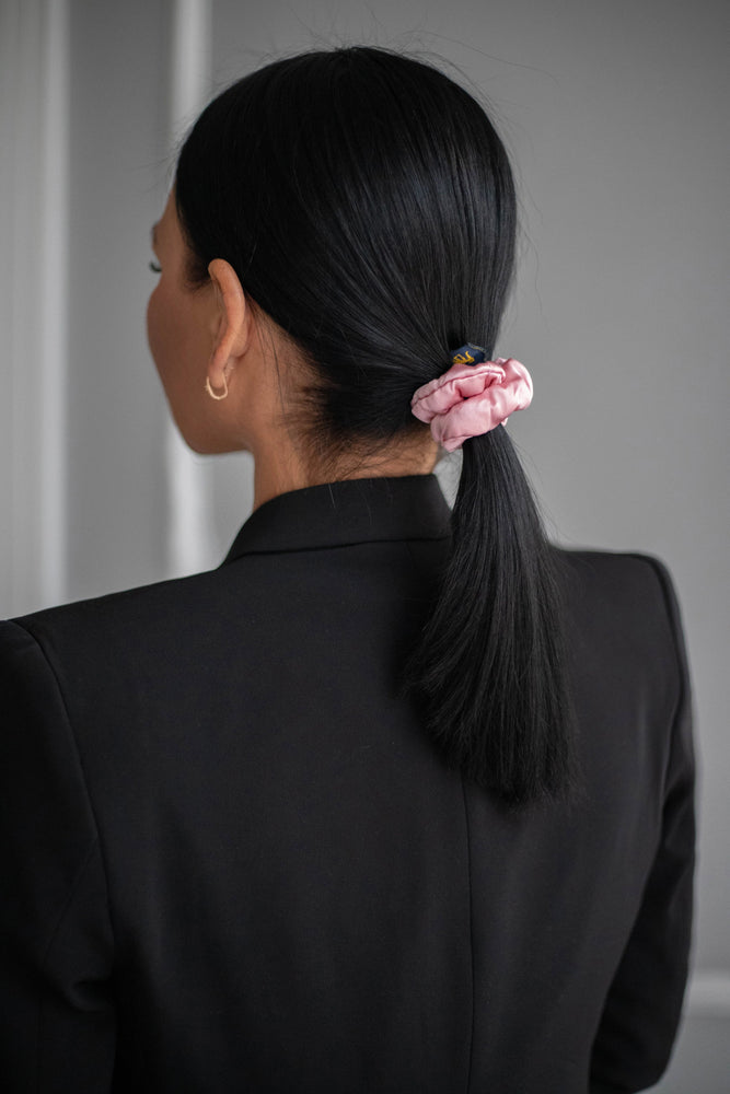 
                  
                    A black-haired woman, view from the back, with stylish ponytail is wearing Malkiele designer pink silk-covered coil scrunchie, name Grace.
                  
                