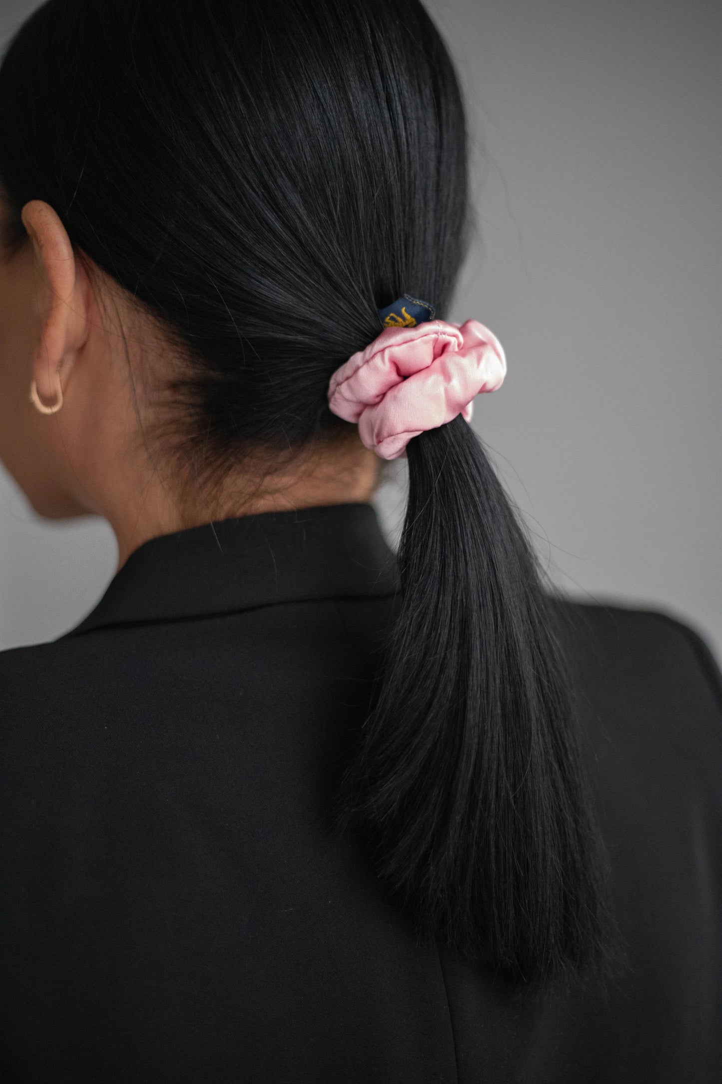 
                  
                    A black-haired woman, view from the back, with stylish ponytail is wearing Malkiele designer pink silk-covered coil scrunchie, name Grace.
                  
                