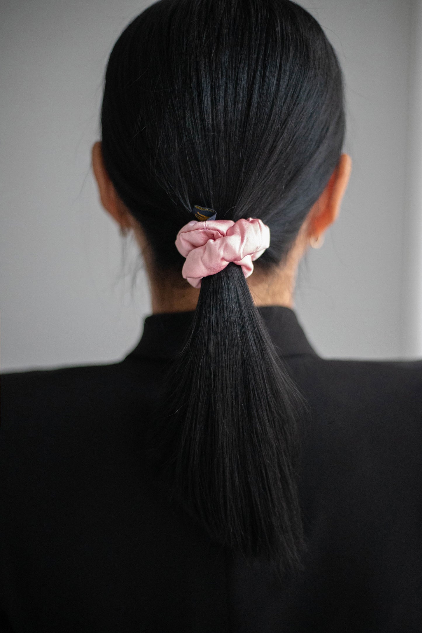 
                  
                    A black-haired woman, view from the back, with stylish ponytail is wearing Malkiele designer pink silk-covered coil scrunchie, name Grace.
                  
                