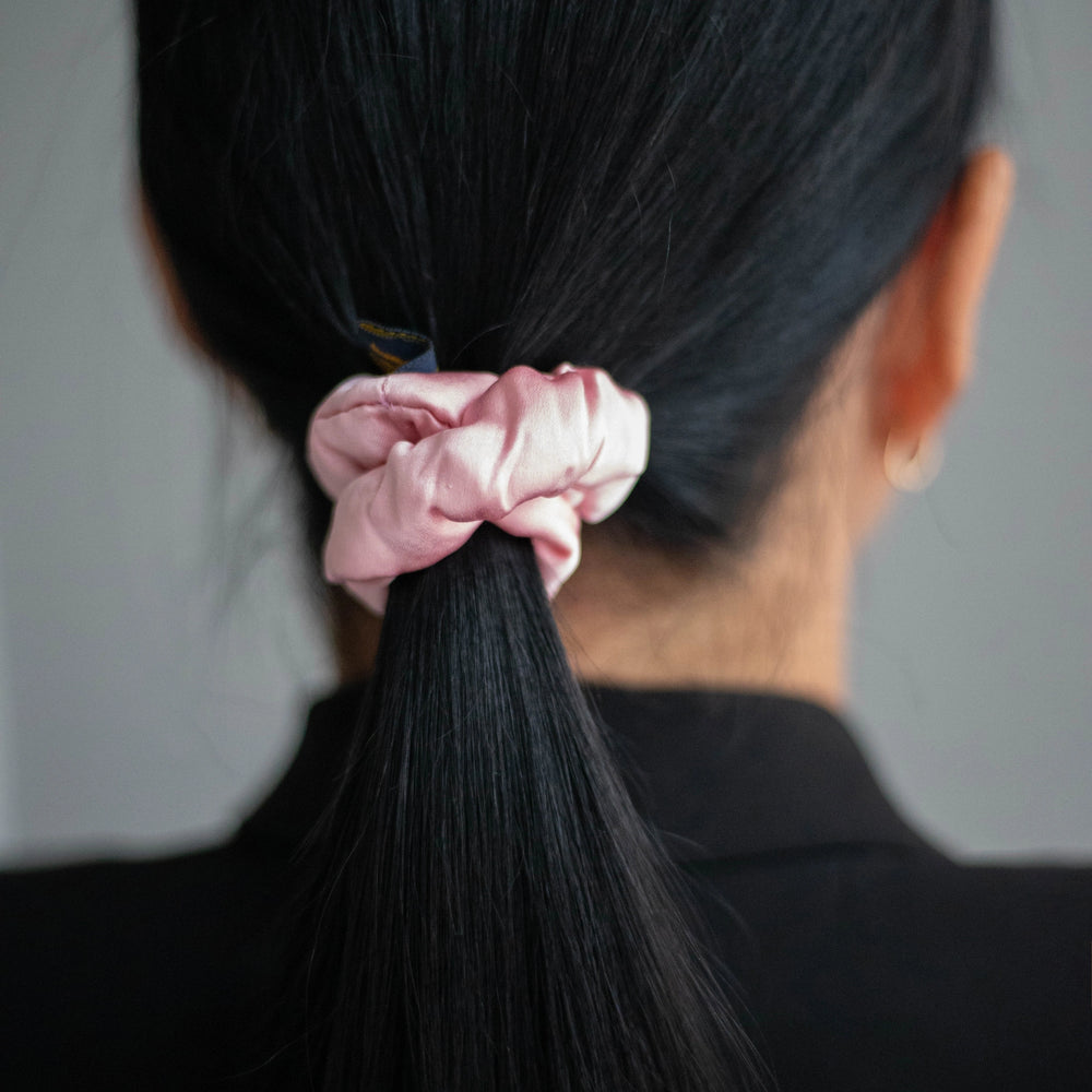 
                  
                    A black-haired woman, view from the back, with stylish ponytail is wearing Malkiele designer pink silk-covered coil scrunchie, name Grace.
                  
                