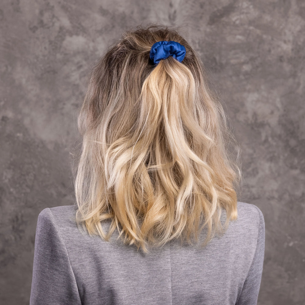 
                  
                    A blonde-haired woman, view from the back,  with stylish ponytail is wearing Malkiele designer light blue silk-covered coil scrunchie, name Grace.
                  
                