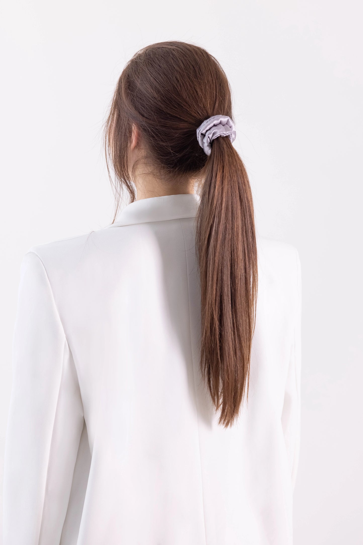 
                  
                    A dark-haired woman, back view,  with stylish ponytail is wearing Malkiele designer grey silk-covered coil scrunchie, name Grace.
                  
                