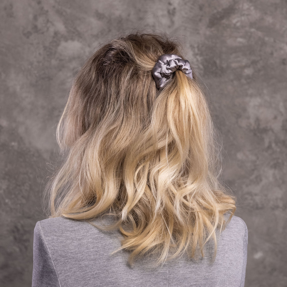 A blonde-haired woman, view from the back,  with stylish ponytail is wearing Malkiele designer grey silk-covered coil scrunchie, name Grace.