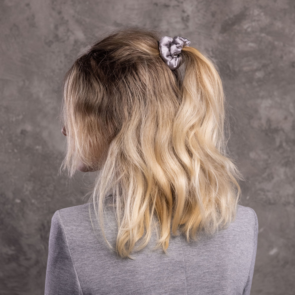 
                  
                    A blonde-haired woman, view from the back,  with stylish ponytail is wearing Malkiele designer grey silk-covered coil scrunchie, name Grace.
                  
                