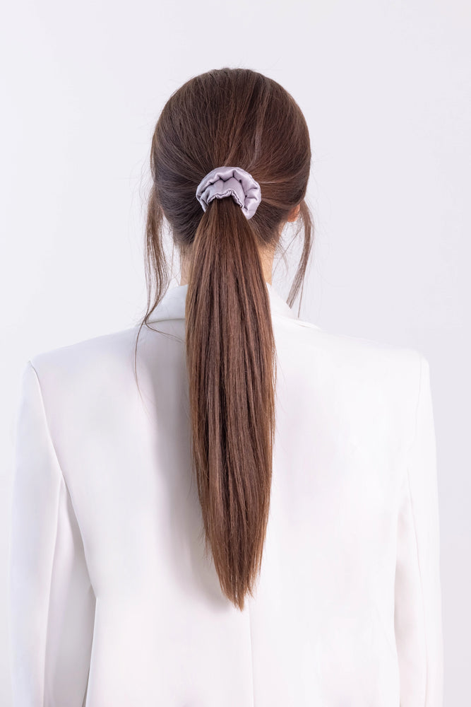 
                  
                    A dark-haired woman, back view,  with stylish ponytail is wearing Malkiele designer grey silk-covered coil scrunchie, name Grace.
                  
                