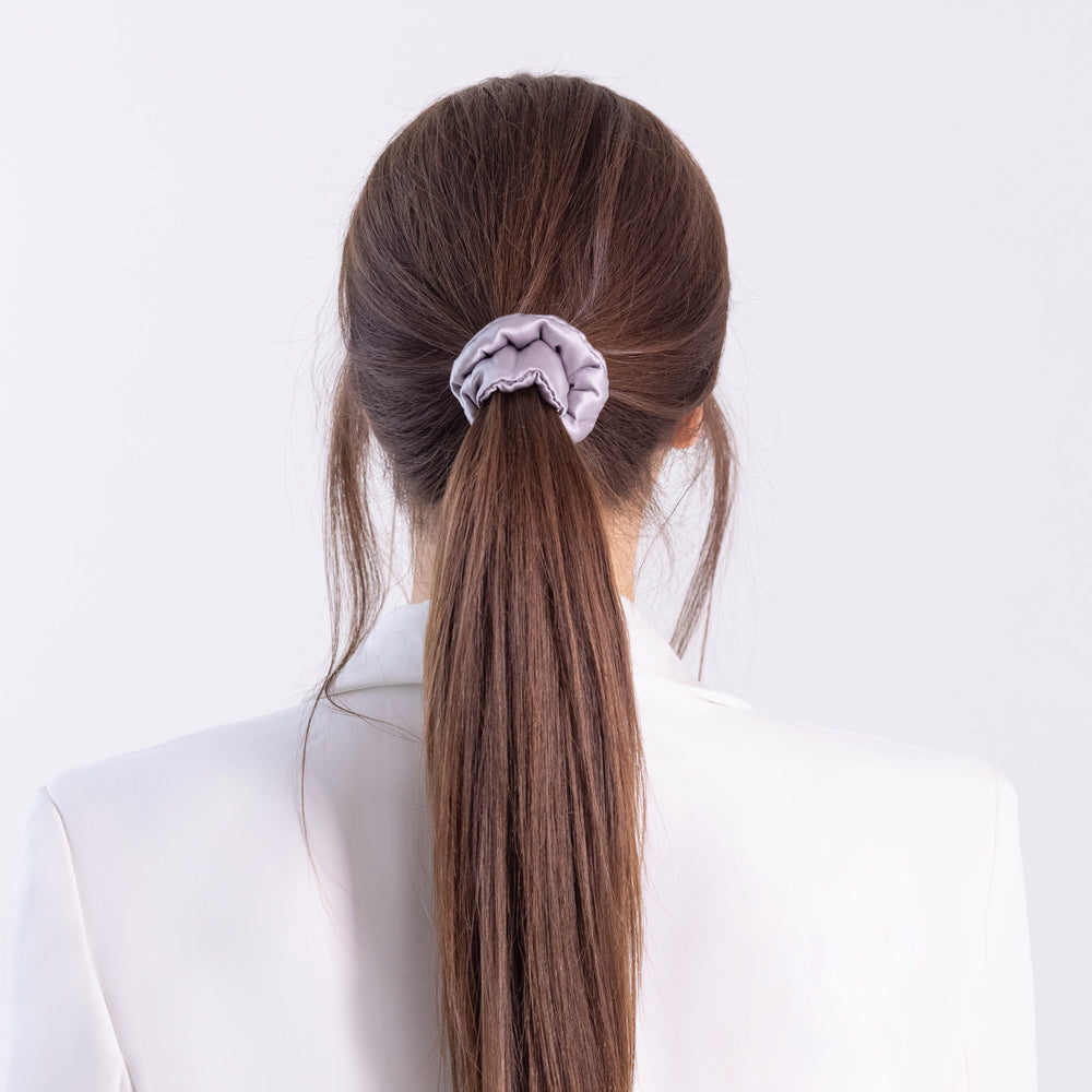 
                  
                    A dark-haired woman, back view,  with stylish ponytail is wearing Malkiele designer grey silk-covered coil scrunchie, name Grace.
                  
                