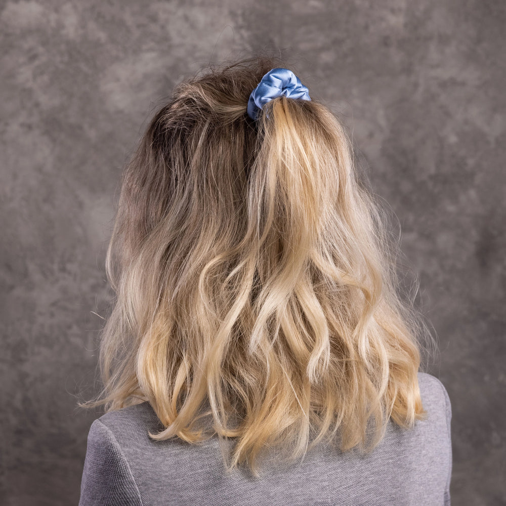 
                  
                    A blonde-haired woman, view from the back,  with stylish ponytail is wearing Malkiele designer light blue silk-covered coil scrunchie, name Grace.
                  
                