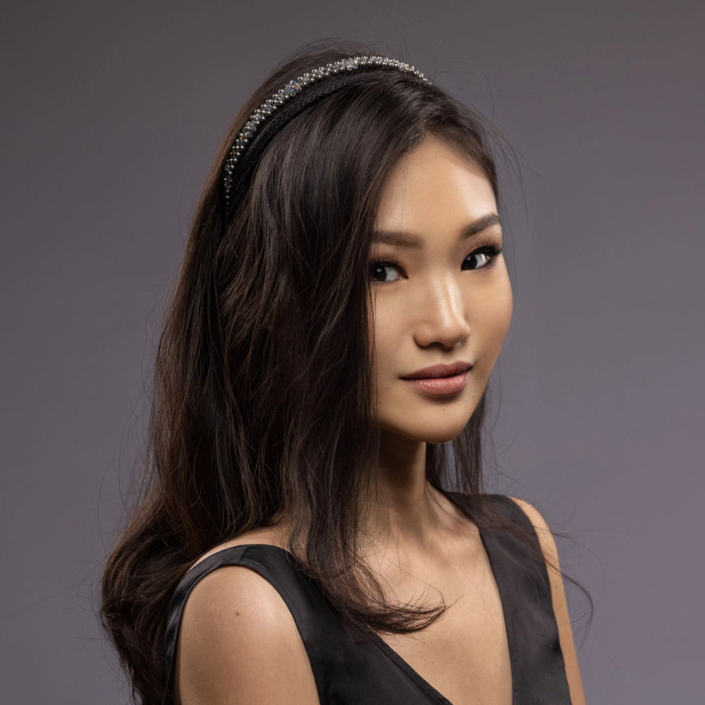 
                  
                    A dark-haired smiling Asian girl is wearing Malkiele designer black silk knit headbands, embellished with pearls from Swarovski, name Victorious.
                  
                