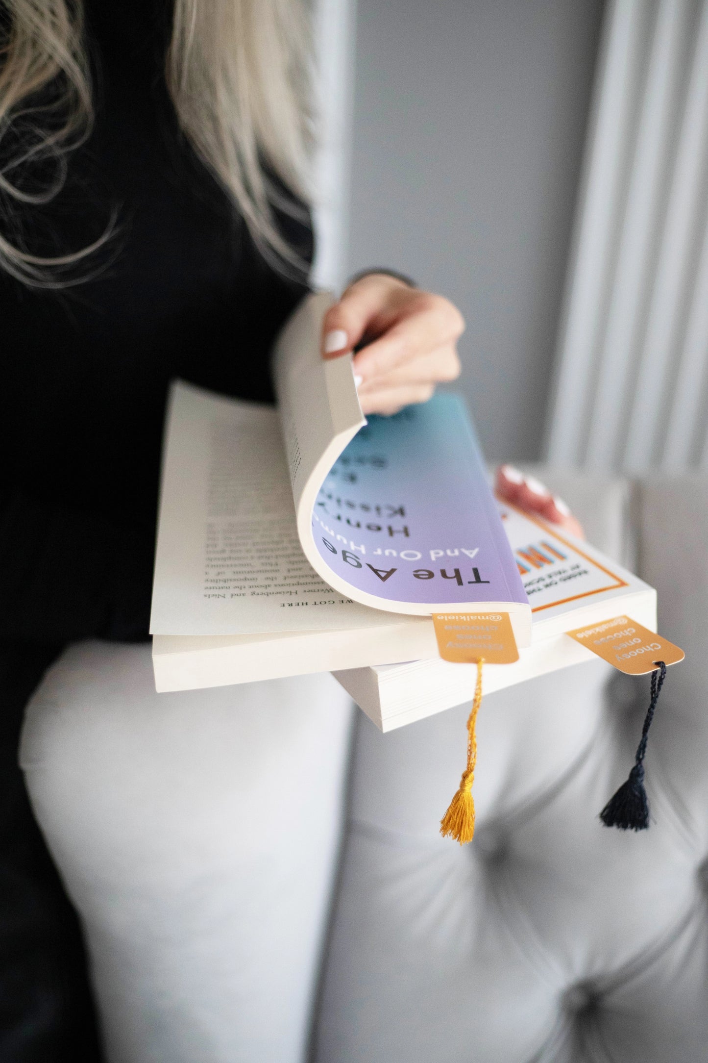 
                  
                    Woman’s hands are holding a book with two Malkiele designer Bookmarks with  silk tassel, name Witty.
                  
                