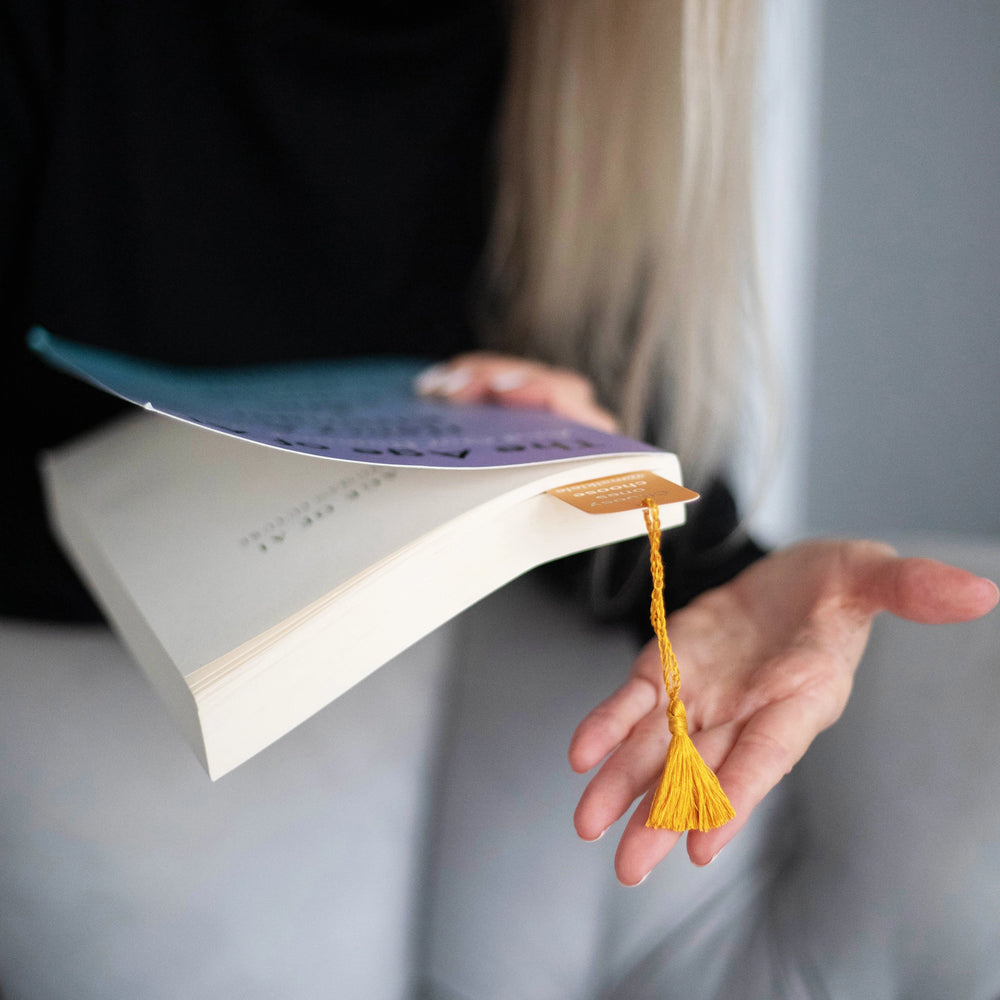 
                  
                    Woman’s hands are holding a book with Malkiele designer Bookmark with yellow silk tassel, name Witty.
                  
                