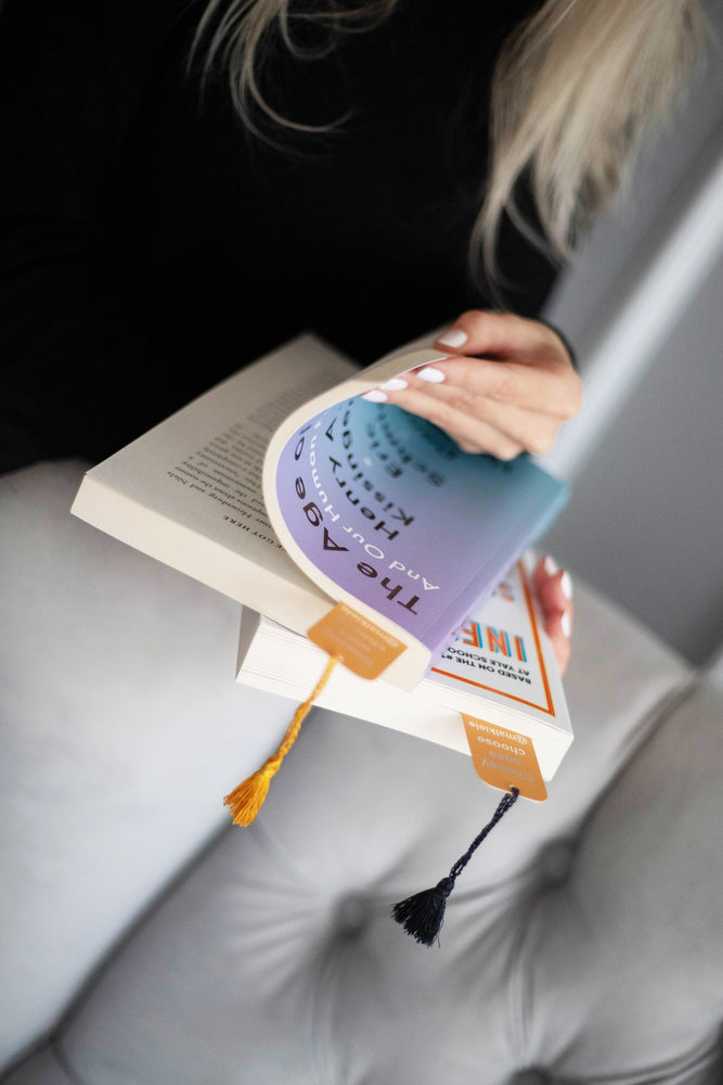 
                  
                    Woman’s hands are holding the books with two Malkiele designer Bookmarks with  silk tassel, name Witty.
                  
                