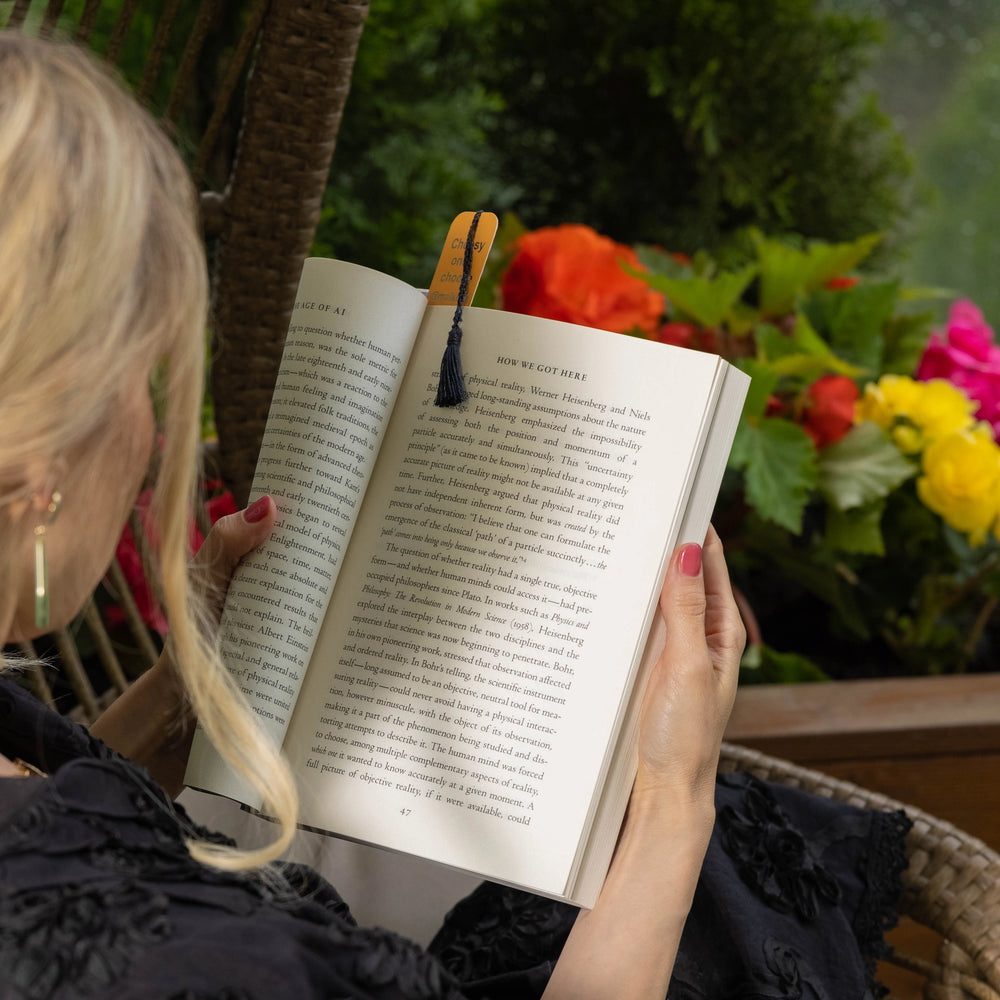 
                  
                    A blonde-haired girl is holding an open book with Malkiele designer Bookmark with navy blue silk tassel, name Witty.
                  
                